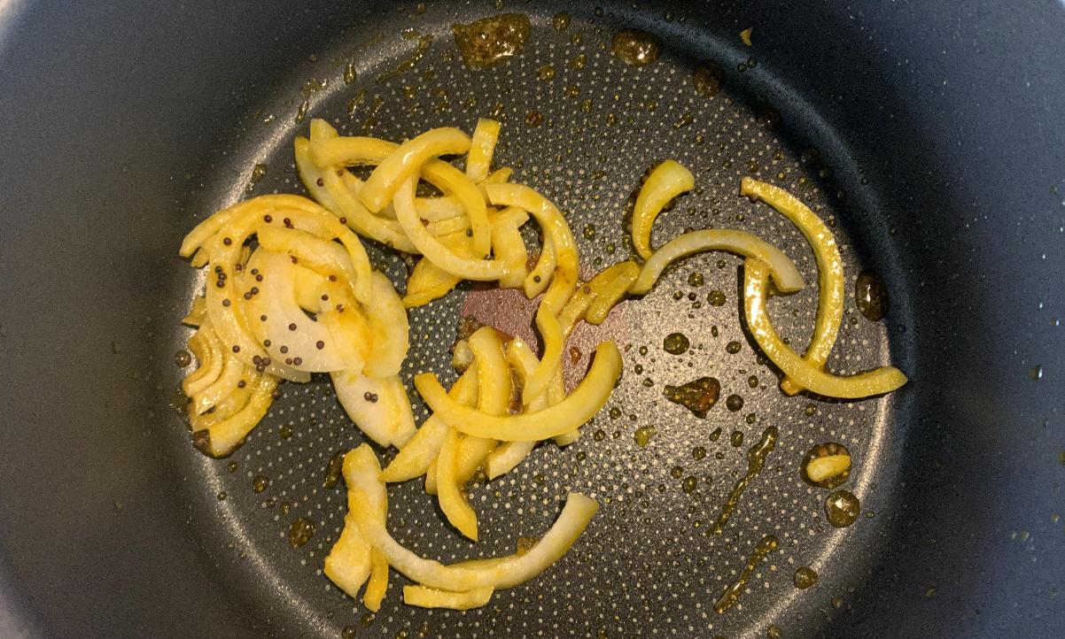 black mustard seeds frying with onion slices in a pan