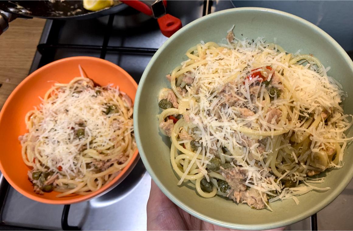 two bowls of spaghetti with capers, tuna and chillis, garnished with parmigiano reggiano