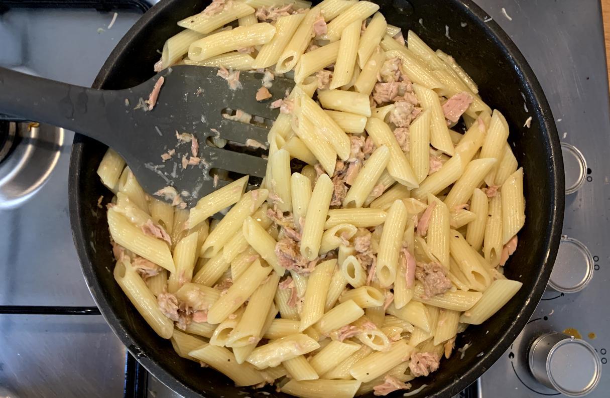 penne pasta and tuna being stirred with a spatula in a pan