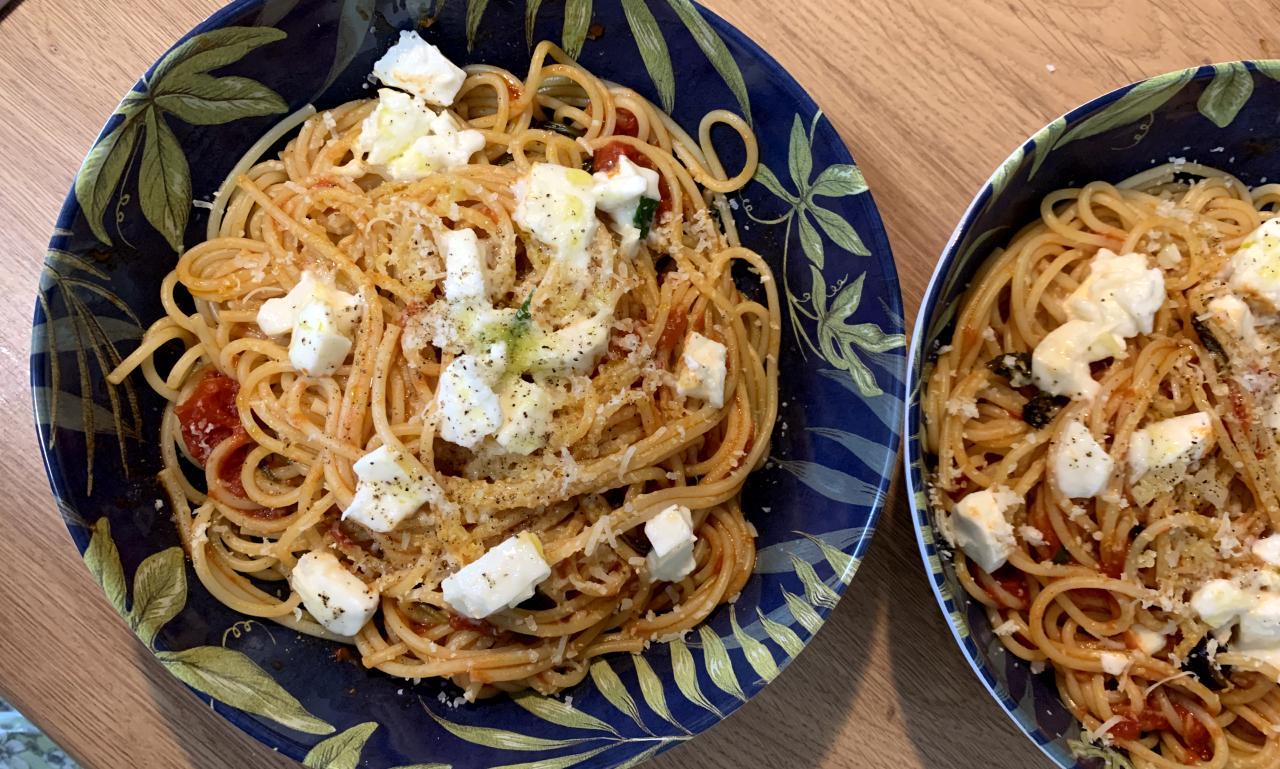 a bowl of spaghetti with a sauce of tomatoes, olives, basil and mozzarella. Pepper is sprinkled on top