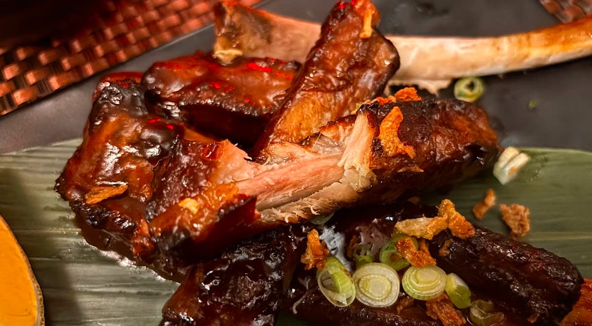 sticky pork ribs with a bite taken out of the side, revealing render meat and a bone