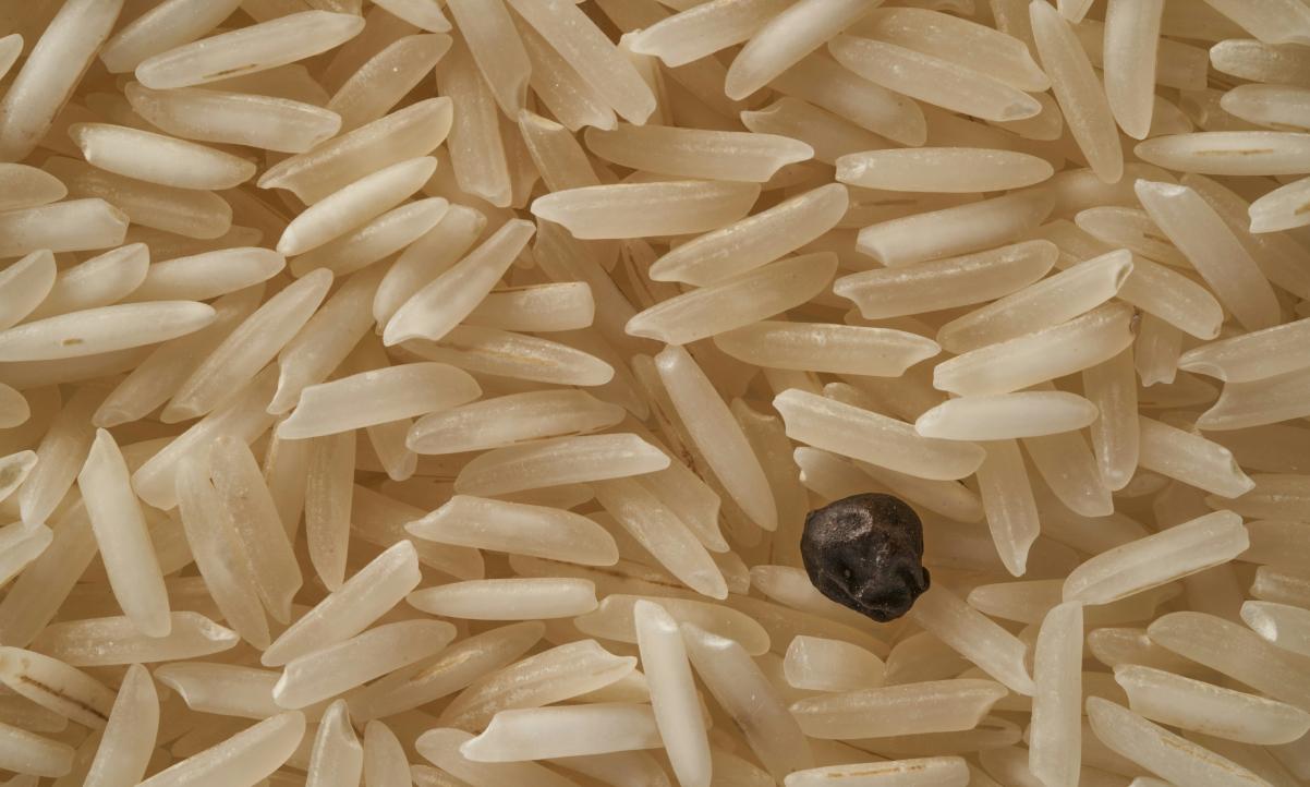 a closeup of long grain basmati rice, uncooked, and a black peppercorn