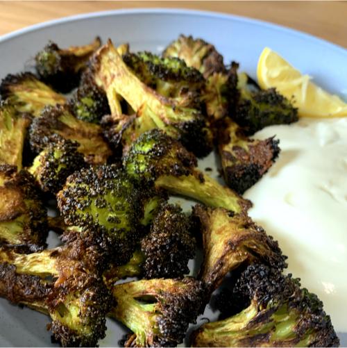 roasted broccoli seasoned with spices on a plate with greek yoghurt and a lemon wedge