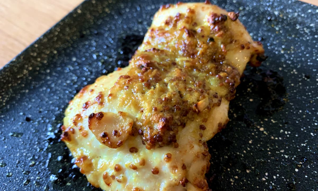 roasted chicken thigh fillet covered in a yellow wholegrain mustard sauce on a black baking tray