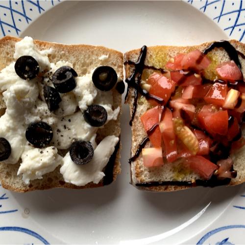 an open bruschetta sandwich with mozzarella, sliced black olives, diced tomatoes and balsamic glaze