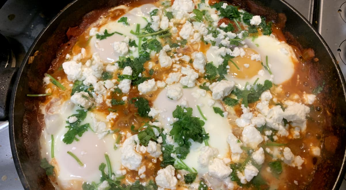 shakshouka for two with several fried eggs garnished with corriander and feta