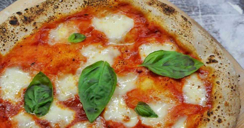 a closeup of a southern Italian pizza neapolitana, garnished with whole fresh basil leaves