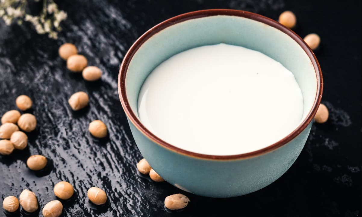 soya beans on a table next to a small blue cup of plant milk