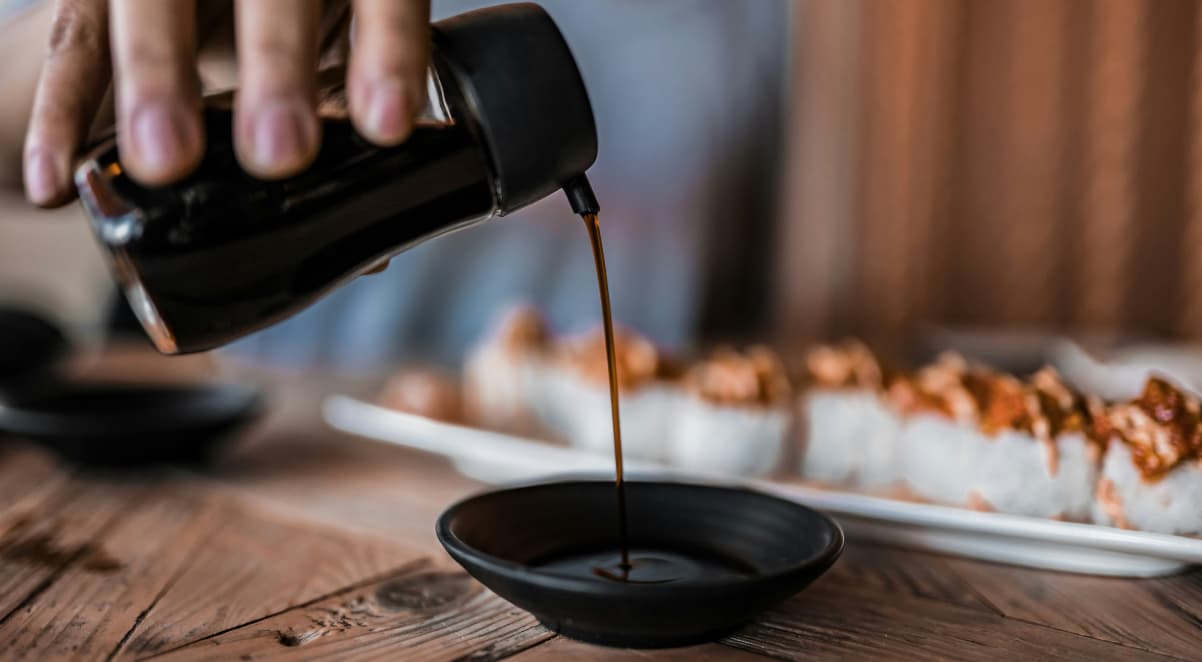 a glass bottle containing soy sauce, pouring into a small black ceramic dish