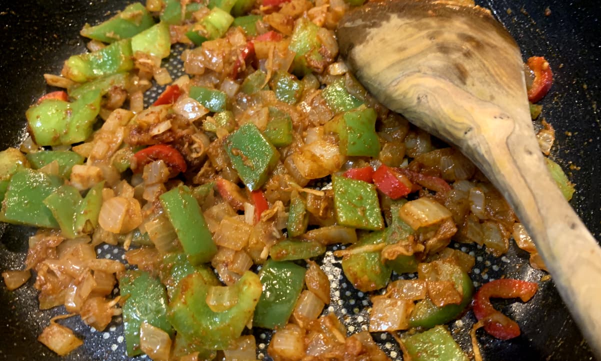 onion, green pepper and red chilli frying in a pan qirh powdered spices