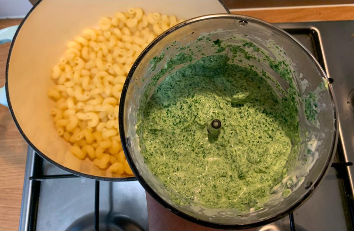 spinach and cream cheese pasta sauce in a mini blender. In the background is a large pot containing cooked spirali pasta