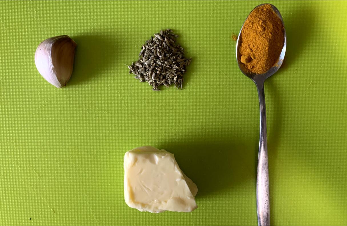 one clove of garlic, a teaspoon of fennel seeds, a teaspoon of turmeric and a knob of butter arranged on a chopping board