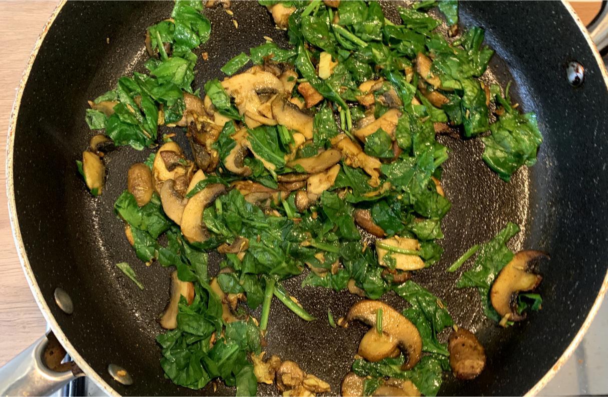 spinach and mushrooms frying in a pan