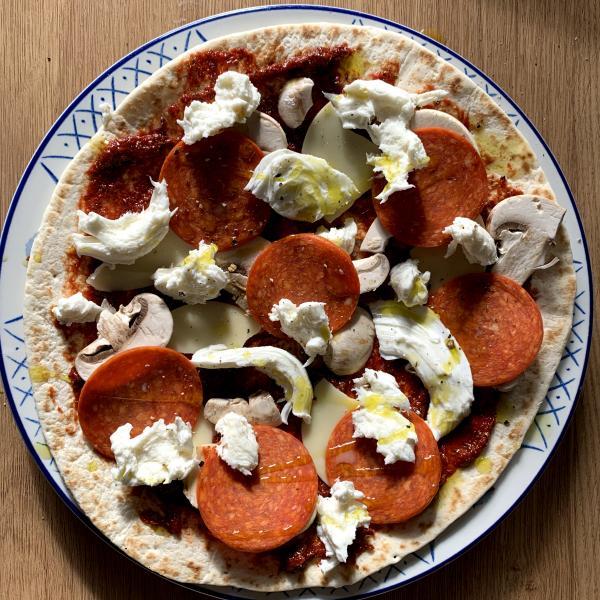 an uncooked tortilla pizza, adorned with tomato puree pizza sauce, cheese, sliced mushrooms and pepperoni