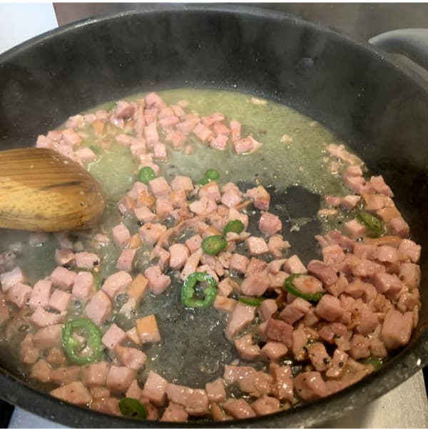 bacon lardons, wine and chilli slices frying in a pan 