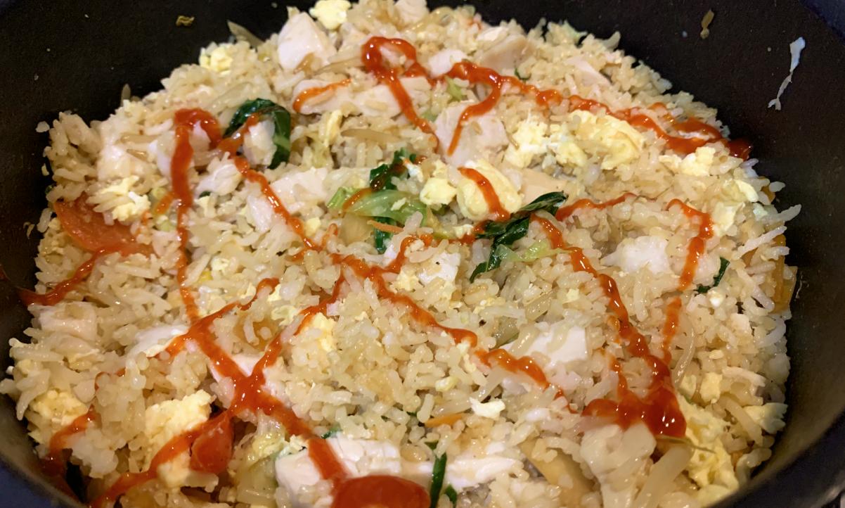 chicken and egg fried rice with sriracha squirted on top in a zig zag pattern