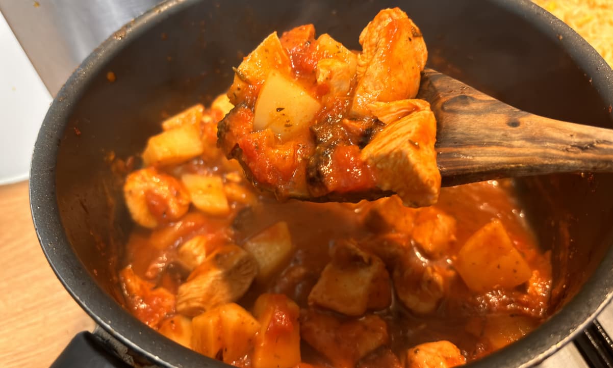 chicken and potato stew in a pot, some of which is held up by a wooden spoon in the foreground