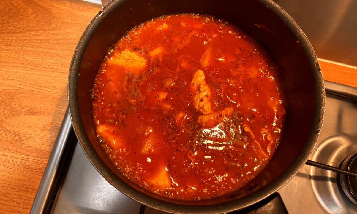 red coloured liquid in a black cooking pot containing chicken and potato stew