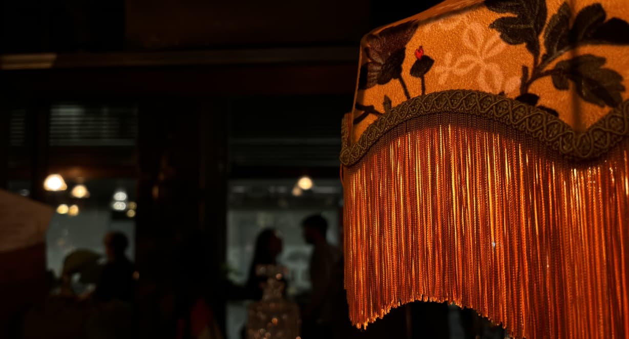 interior of The Duke's Umbrella with a tasseled orange lampshade in the foreground and silhouetted diners in the dark background