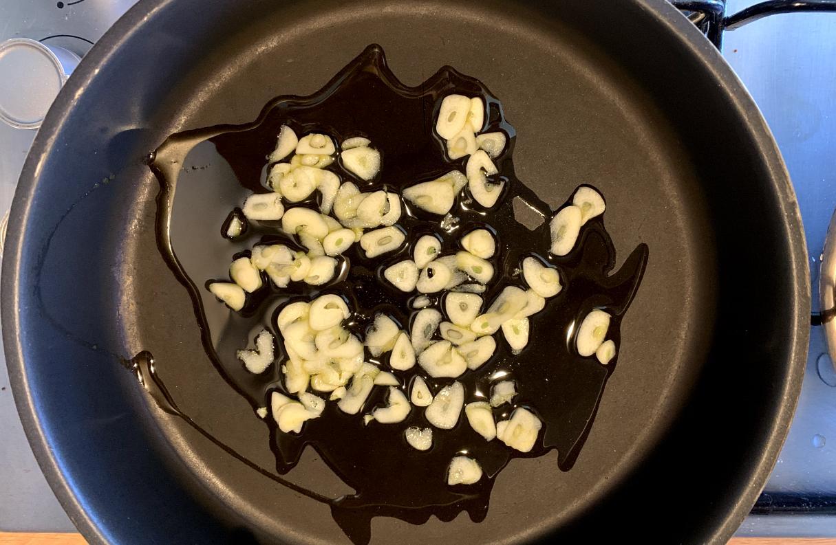 thinly slices garlic frying in oil in a wide frying pan