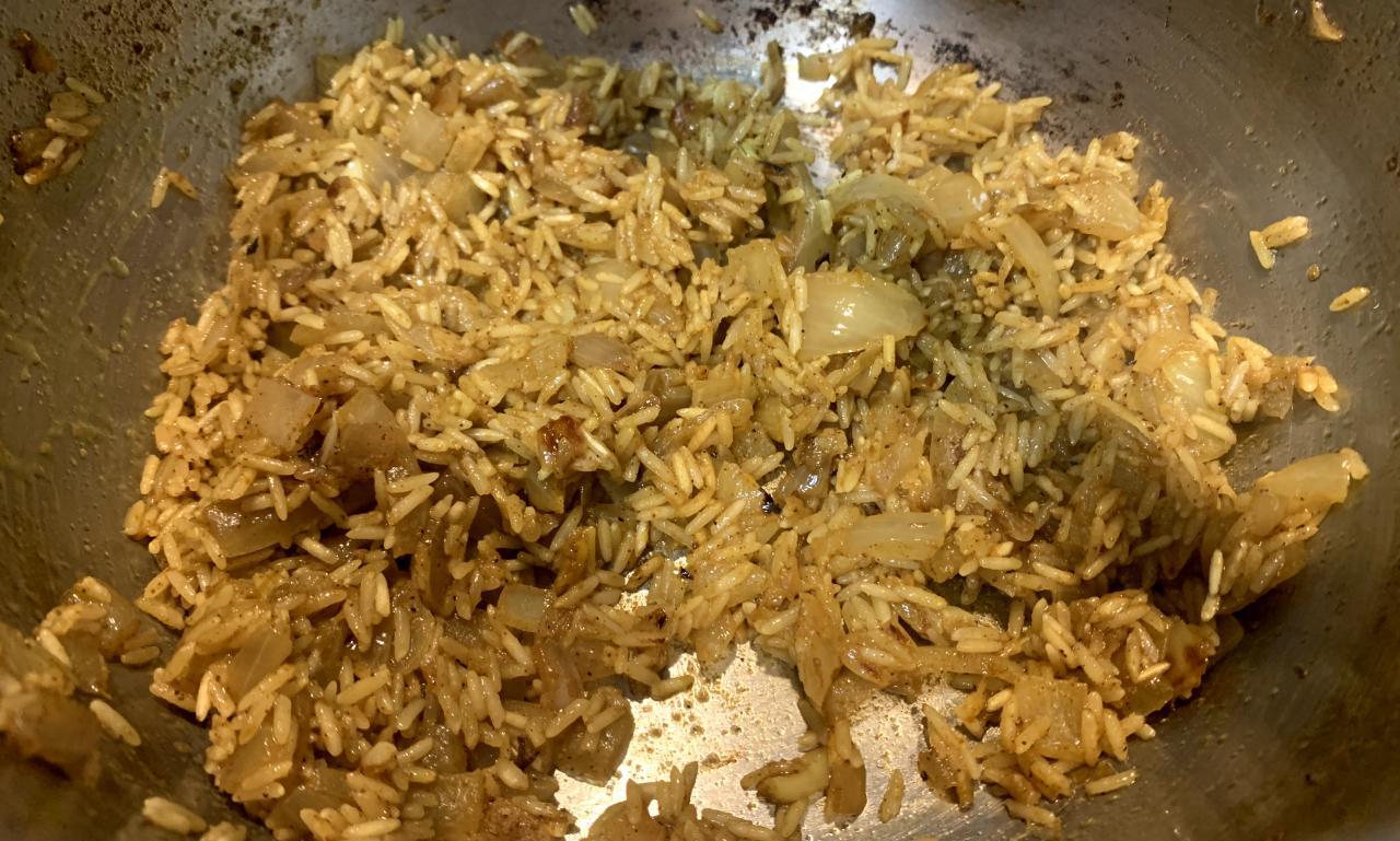 yellow-tinged basmati rice toasting in the bottom of a saucepan with oil, onion and spices