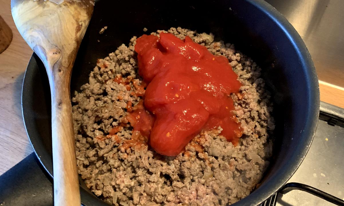 cooked mince in a pot, with some tinned plum tomatoes on top