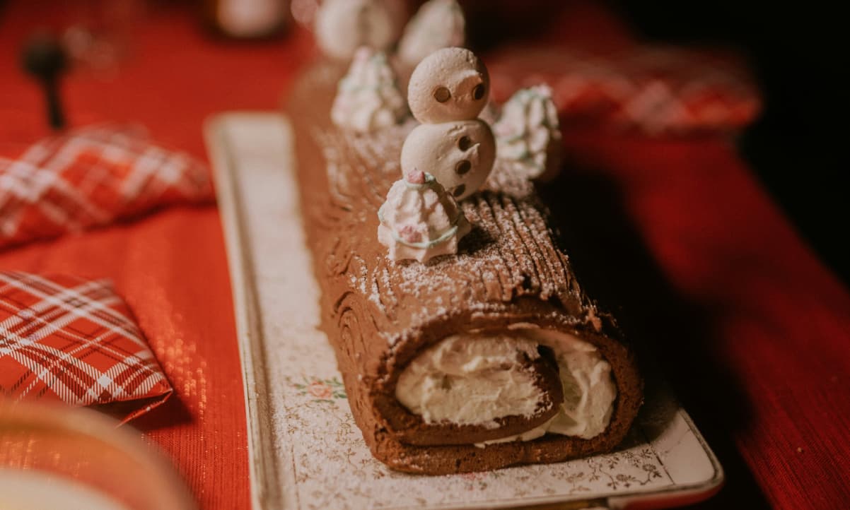 a chocolate, cream filled yule log decorated with whipped cream and a snowman