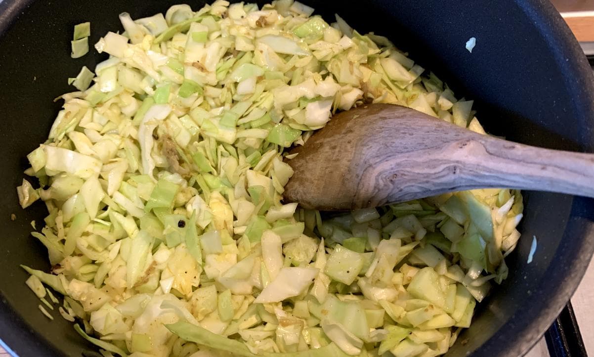 chopped cabbage being stirred in a pot with black pepper