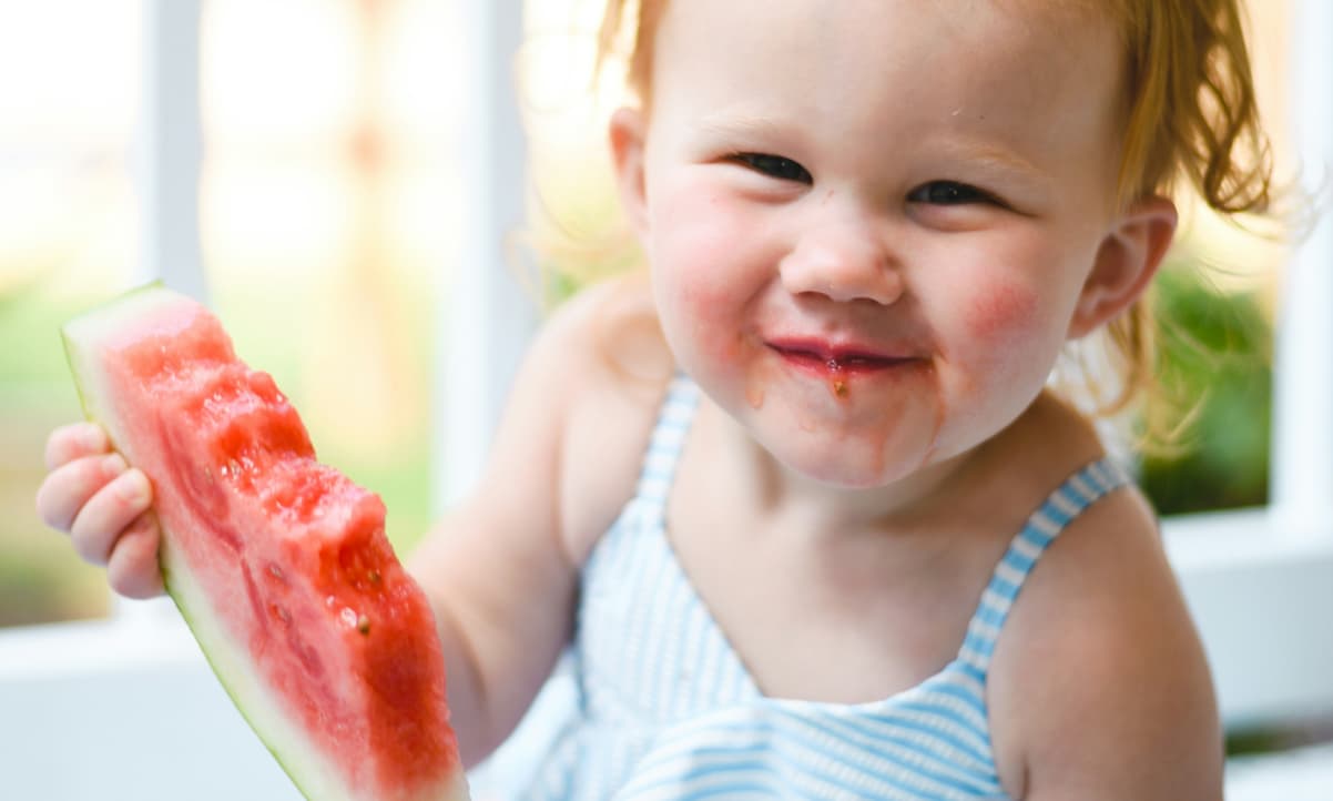 a happy baby holding a watermelon doing baby led weaning